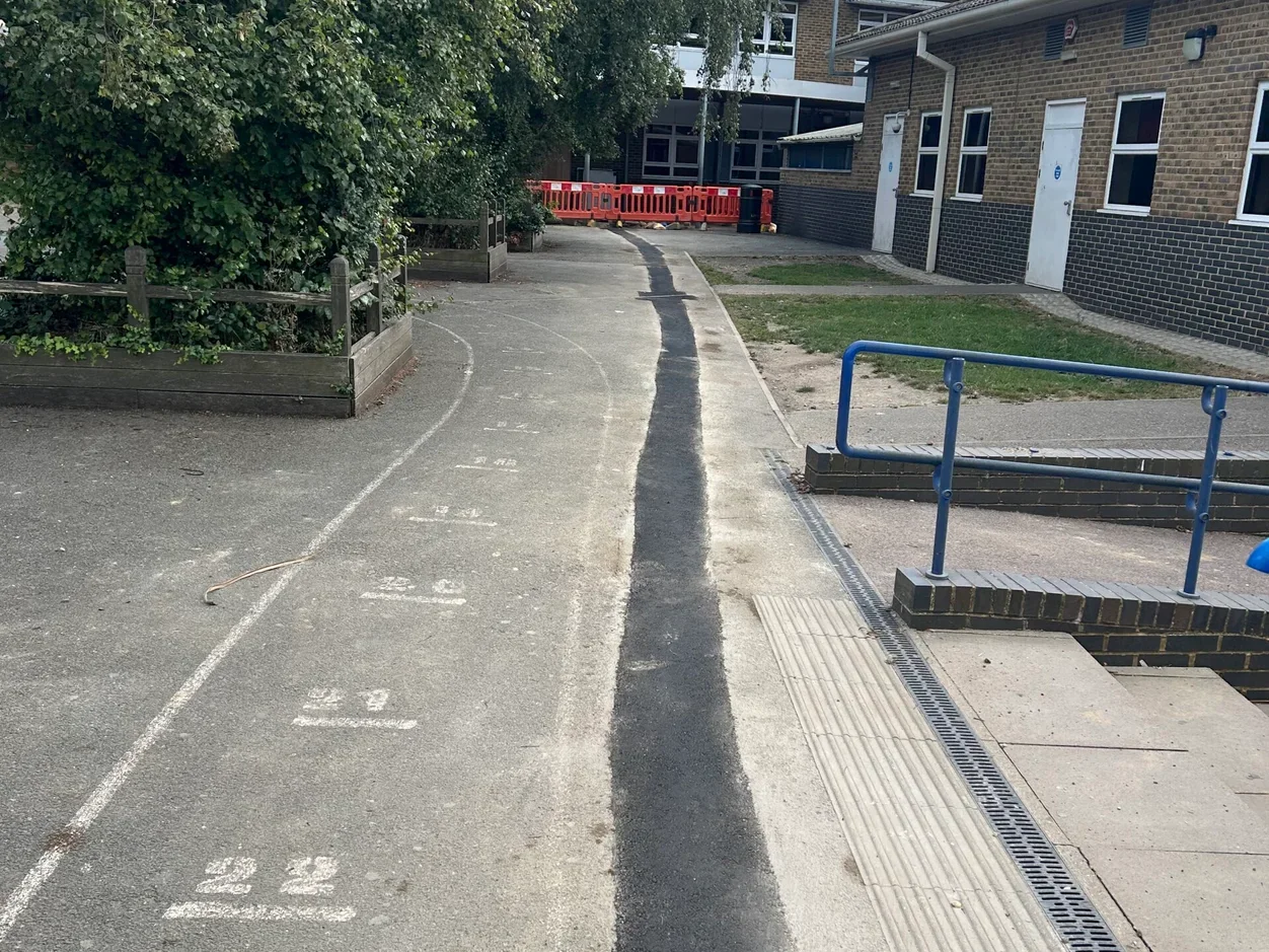 Freshly laid tarmac resurfacing strip alongside older concrete paving on a groundworks job